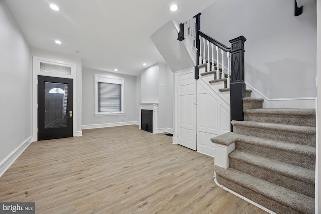 foyer entrance featuring baseboards, stairway, recessed lighting, a fireplace, and light wood-style floors