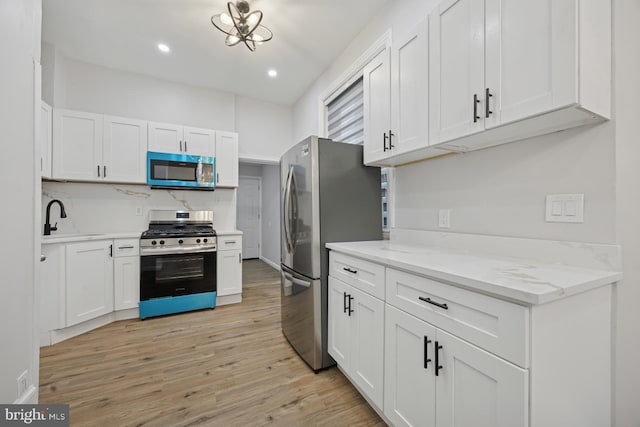 kitchen featuring light stone countertops, light wood finished floors, a sink, stainless steel appliances, and white cabinets