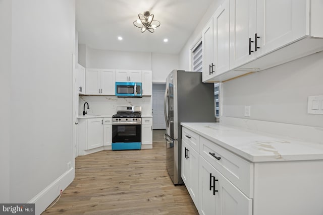 kitchen featuring a sink, tasteful backsplash, white cabinetry, stainless steel appliances, and light wood-style floors