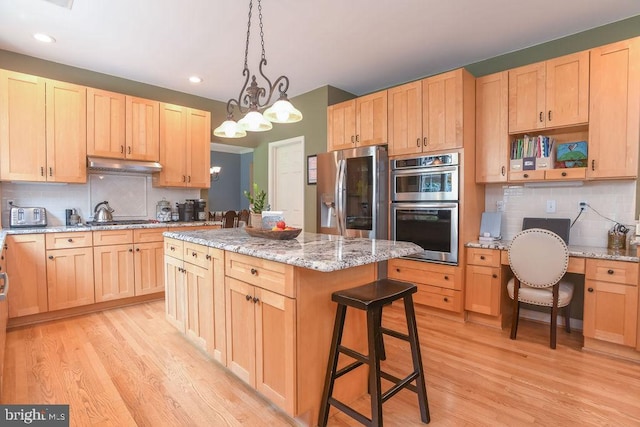 kitchen with light brown cabinets, a center island, under cabinet range hood, light wood-type flooring, and appliances with stainless steel finishes