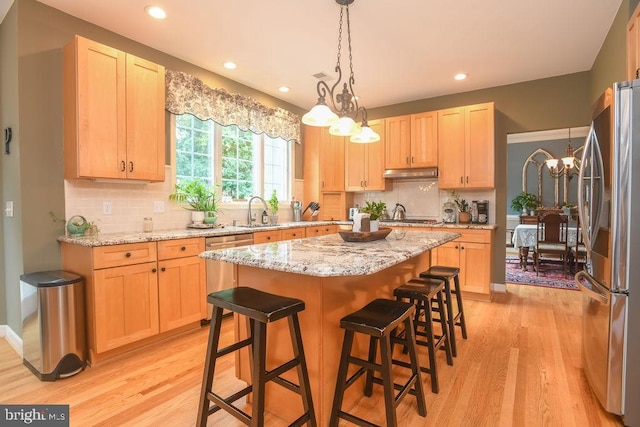 kitchen with light brown cabinets, under cabinet range hood, a sink, stainless steel appliances, and a chandelier