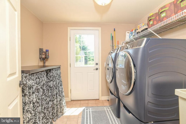 clothes washing area with light tile patterned flooring, laundry area, washing machine and dryer, and baseboards