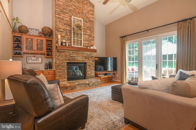 living area featuring a stone fireplace, high vaulted ceiling, wood finished floors, and ceiling fan