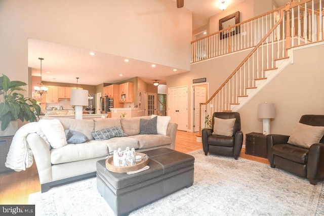 living area with light wood-style flooring, recessed lighting, stairway, a high ceiling, and an inviting chandelier