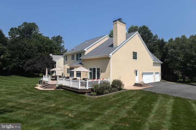 rear view of property featuring stucco siding, a chimney, driveway, a yard, and an attached garage