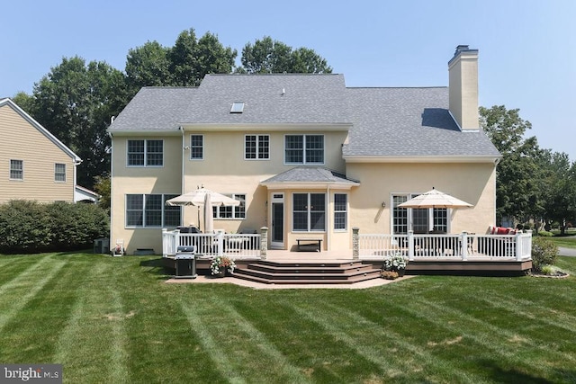 rear view of house with a deck, stucco siding, a chimney, and a yard