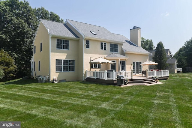 back of house featuring a wooden deck, a lawn, a chimney, and stucco siding