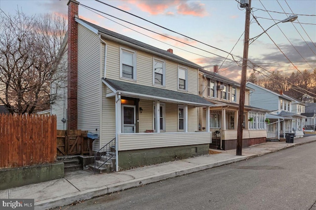 multi unit property featuring a residential view, covered porch, a chimney, and fence