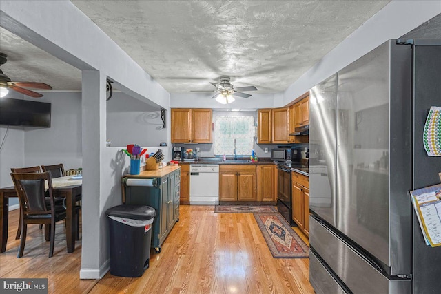 kitchen with under cabinet range hood, light wood finished floors, black appliances, and a sink