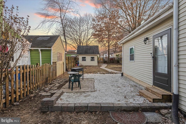 patio terrace at dusk featuring a storage shed, an outbuilding, a fenced backyard, and entry steps