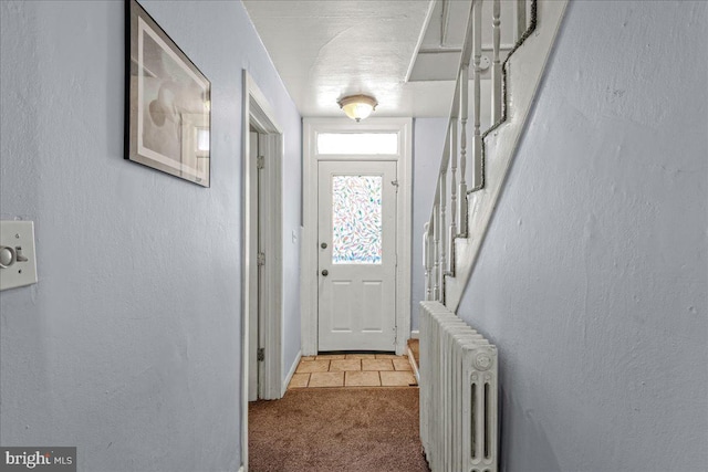 entryway with a textured wall, carpet flooring, radiator heating unit, and stairway