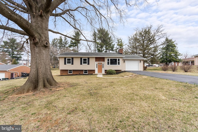 split foyer home featuring aphalt driveway, a front lawn, a garage, and a chimney