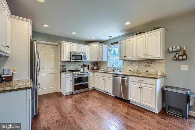 kitchen with backsplash, appliances with stainless steel finishes, dark wood-style floors, white cabinets, and a sink