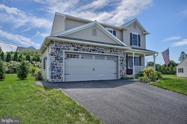 traditional-style home with a front yard, covered porch, a garage, stone siding, and driveway