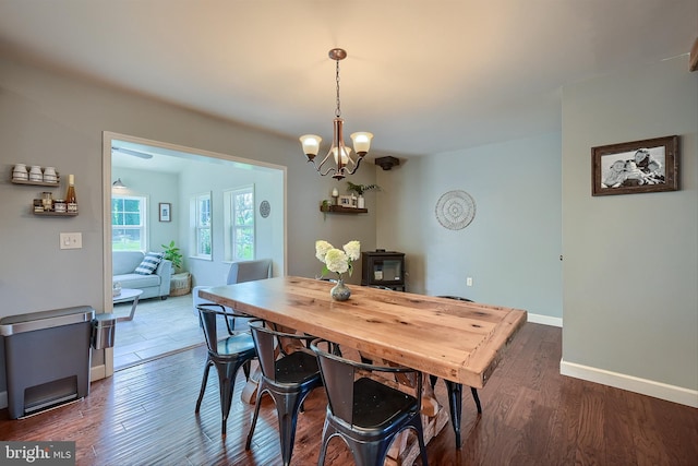 dining area with a wood stove, baseboards, a chandelier, and dark wood-style flooring