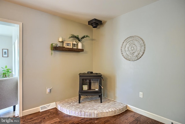 living area with visible vents, a wood stove, baseboards, and wood finished floors