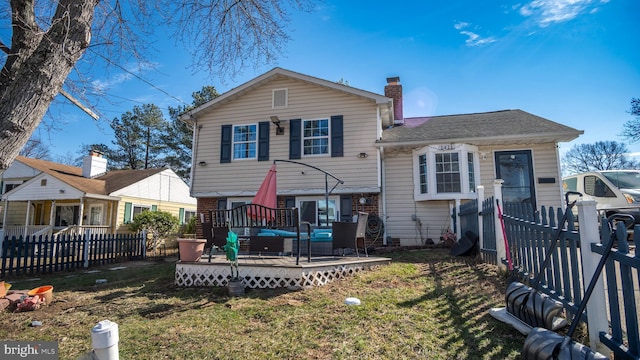 split level home with a wooden deck, a fenced backyard, a chimney, a front lawn, and brick siding