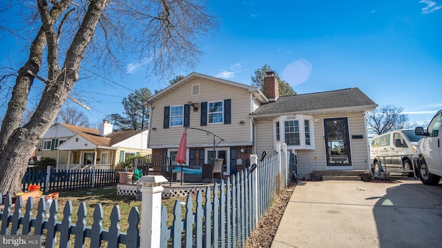 split level home with a fenced front yard, a chimney, and roof with shingles