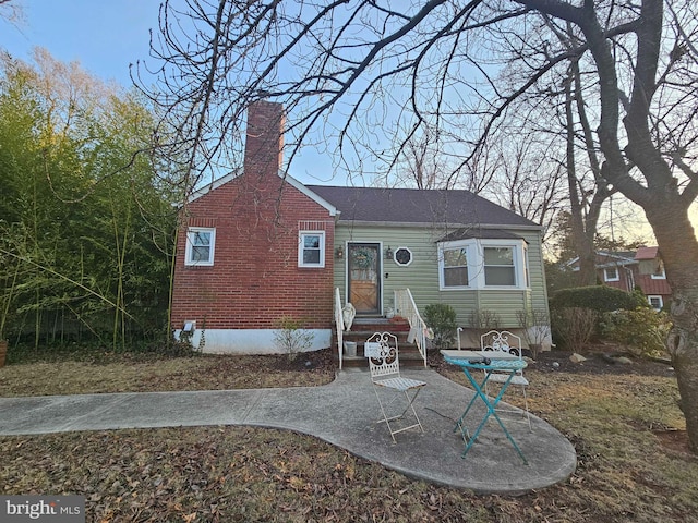 view of front of home with brick siding, a chimney, and entry steps