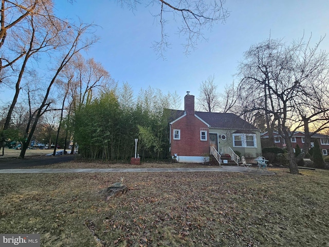 view of side of property with brick siding, a lawn, a chimney, and entry steps