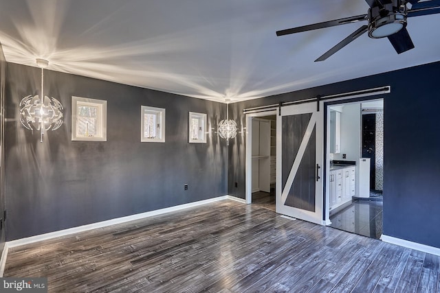 unfurnished bedroom with a barn door, dark wood-style floors, baseboards, and connected bathroom