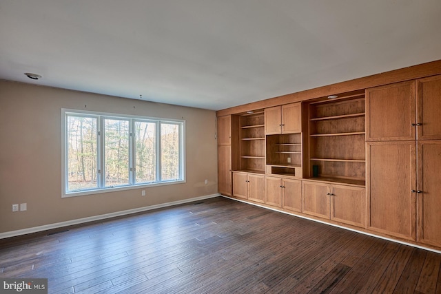 unfurnished living room with baseboards and dark wood-type flooring