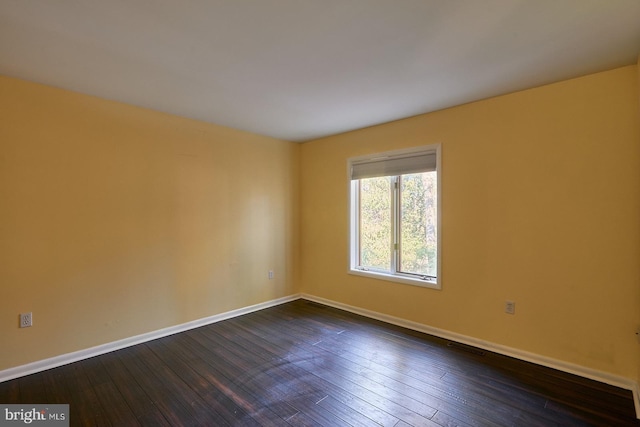 spare room featuring dark wood finished floors, visible vents, and baseboards