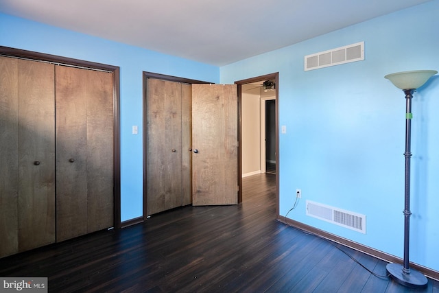 unfurnished bedroom featuring visible vents, baseboards, two closets, and dark wood-style flooring