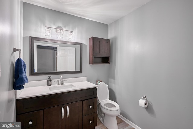 bathroom featuring baseboards, toilet, wood finished floors, and vanity