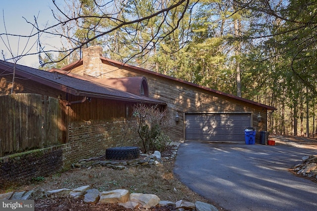 view of property exterior featuring a garage, brick siding, a chimney, and driveway