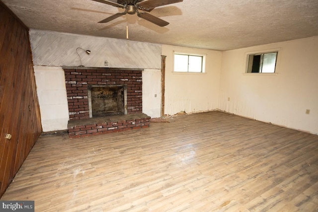 unfurnished living room with a fireplace, wood finished floors, a ceiling fan, and a textured ceiling