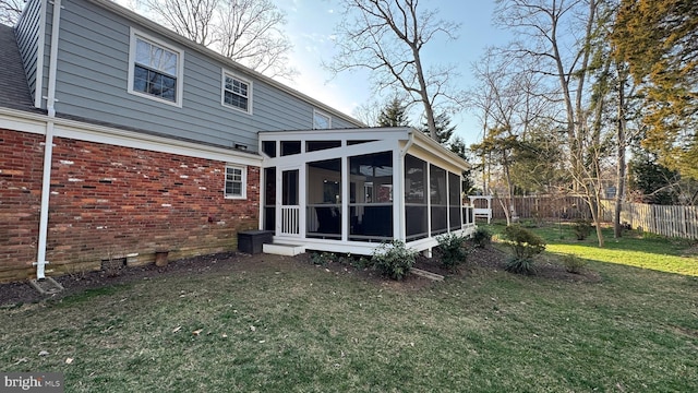 back of house featuring a yard, a sunroom, brick siding, and fence