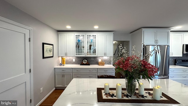 kitchen with backsplash, glass insert cabinets, light stone counters, freestanding refrigerator, and white cabinetry