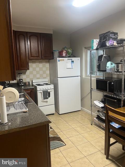 kitchen with dark countertops, white appliances, light tile patterned floors, decorative backsplash, and dark brown cabinets