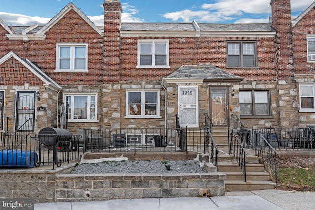 multi unit property featuring stone siding, a chimney, and fence