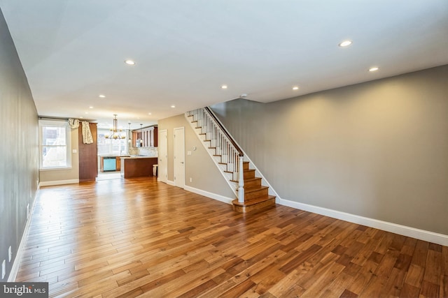 unfurnished living room featuring a notable chandelier, recessed lighting, stairway, and wood finished floors