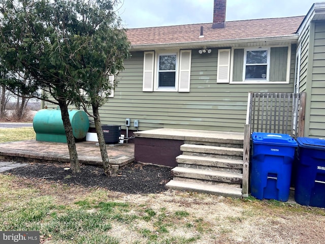 view of side of home with a chimney, a shingled roof, and central AC