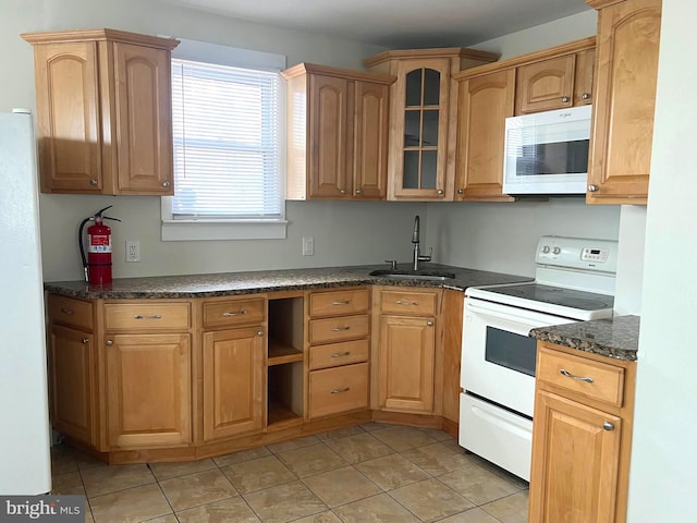 kitchen featuring glass insert cabinets, light tile patterned floors, dark stone countertops, white appliances, and a sink