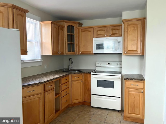 kitchen featuring a sink, dark stone counters, white appliances, light tile patterned floors, and glass insert cabinets