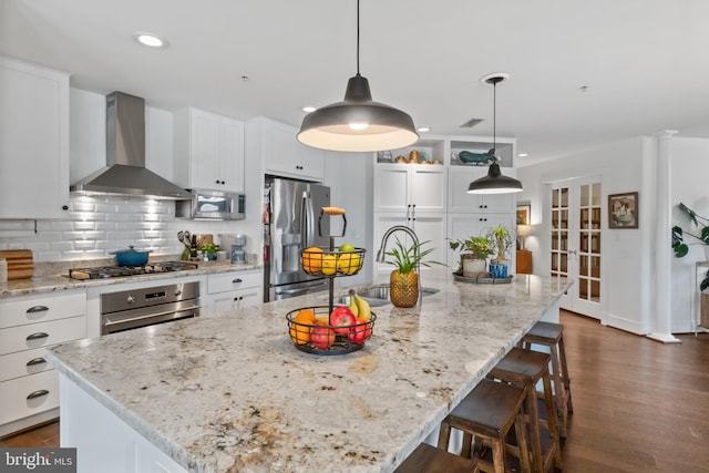 kitchen with a sink, decorative backsplash, appliances with stainless steel finishes, white cabinetry, and wall chimney range hood