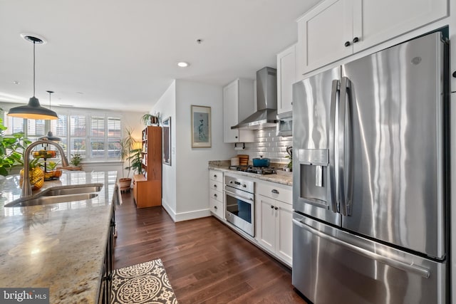 kitchen with a sink, dark wood-type flooring, appliances with stainless steel finishes, wall chimney exhaust hood, and backsplash