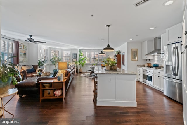 kitchen with visible vents, a kitchen island, dark wood-style flooring, stainless steel appliances, and wall chimney exhaust hood