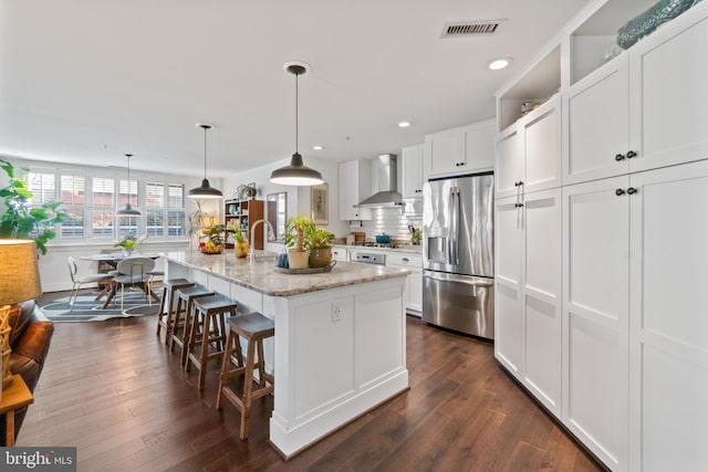 kitchen featuring a kitchen bar, visible vents, stainless steel appliances, wall chimney exhaust hood, and white cabinets