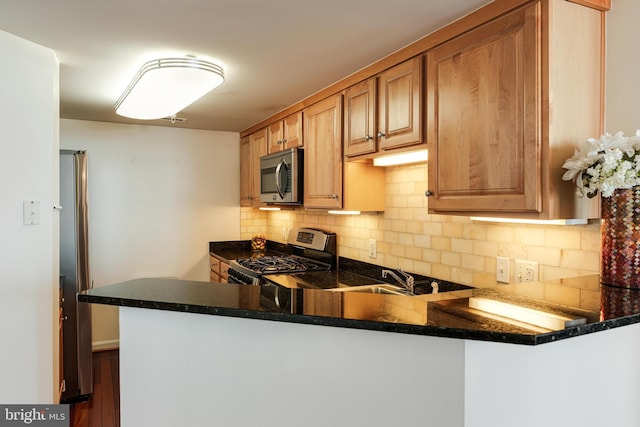 kitchen with dark countertops, backsplash, a peninsula, stainless steel appliances, and a sink