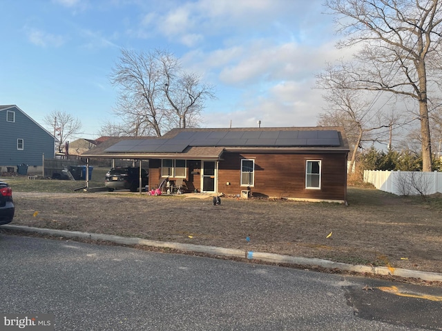 view of front facade with a carport, roof mounted solar panels, and fence