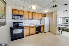 kitchen with black appliances, light countertops, a paneled ceiling, and a sink