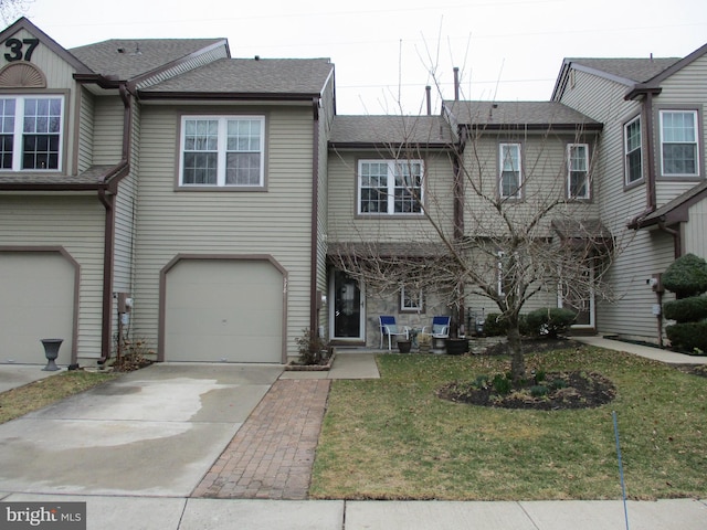 townhome / multi-family property with a garage, concrete driveway, a front lawn, and a shingled roof