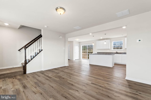 unfurnished living room with stairway, baseboards, visible vents, and wood finished floors