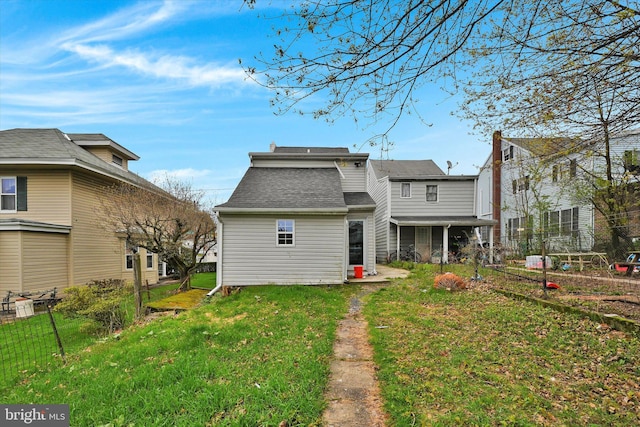 back of house with a lawn, roof with shingles, and fence