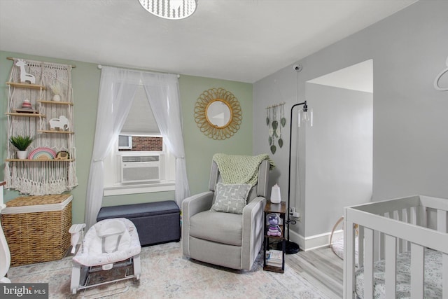 bedroom featuring a nursery area, wood finished floors, baseboards, and cooling unit